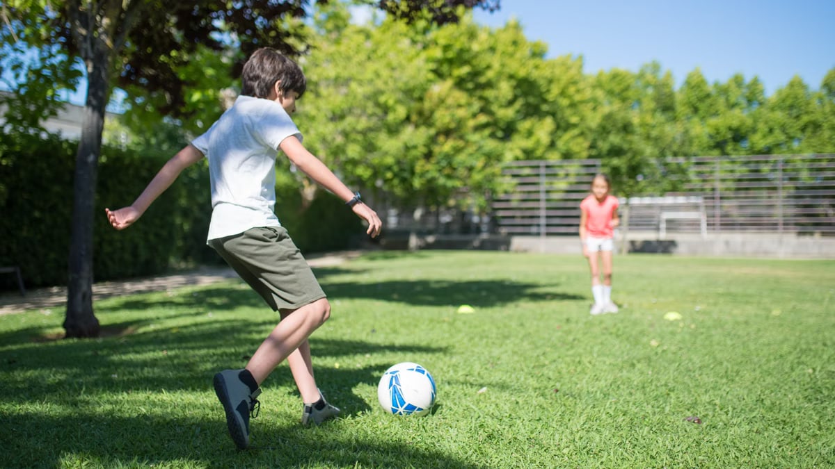 Children enjoying a sunny day playing soccer in a park with lush greenery.